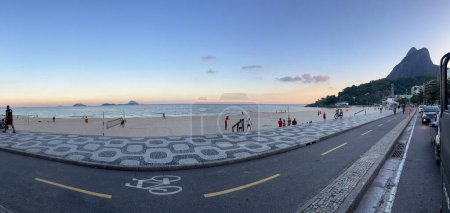 Téléchargez les photos : Rio de Janeiro, Brésil, 06-07-2023 : vue au coucher du soleil de la plage d'Ipanema, l'une des plages les plus célèbres du monde, avec le trottoir graphique emblématique le long de l'Avenida Atlantica (Atlantic Avenue) et Morro Dois Irmaos - en image libre de droit