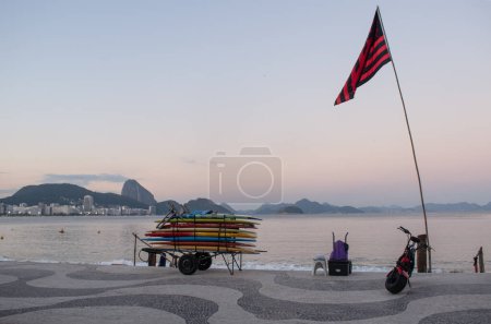 Téléchargez les photos : Rio de Janeiro, Brésil, 07-06-2023 : planches de surf empilées sur un chariot au coucher du soleil sur la plage d'Ipanema, l'une des plages les plus célèbres au monde, avec le trottoir graphique emblématique le long de l'Avenida Atlantica - en image libre de droit