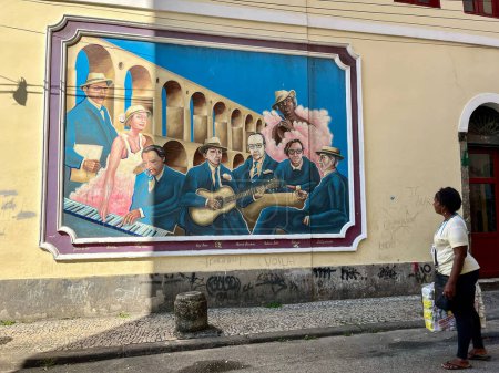 Foto de Río de Janeiro, Brasil, 06-07-2023: mujer en las calles de Lapa mirando un mural dedicado a la música brasileña con el Acueducto Carioca, conocido como Arcos da Lapa y símbolo del distrito, en el fondo - Imagen libre de derechos
