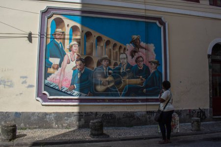 Foto de Río de Janeiro, Brasil, 06-07-2023: mujer en las calles de Lapa mirando un mural dedicado a la música brasileña con el Acueducto Carioca, conocido como Arcos da Lapa y símbolo del distrito, en el fondo - Imagen libre de derechos