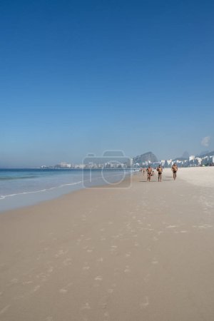 Téléchargez les photos : Rio de Janeiro, Brésil, 06-07-2023 : jogging sur le sable de la plage de Leme, à côté de la plage de Copacabana, avec vue sur les toits de la ville et ses gratte-ciel le long de l'Avenida Atlantica (Atlantic Avenue) - en image libre de droit