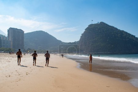 Téléchargez les photos : Rio de Janeiro, Brésil, 06-07-2023 : jogging sur le sable de la plage de Leme, à côté de la plage de Copacabana, avec vue sur les toits de la ville et ses gratte-ciel le long de l'Avenida Atlantica (Atlantic Avenue) - en image libre de droit