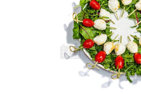 Photo for Charcuterie wreath isolated on white background. Mozzarella, cherry tomatoes, and arugula on skewers. Fashionable snacks, festive vegetarian food, trendy hard light, dark shadow, top view - Royalty Free Image