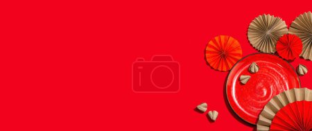 Téléchargez les photos : Happy Chinese New Year table setting concept. Oriental asian style paper fans on red background, minimal concept, flat lay, banner - en image libre de droit