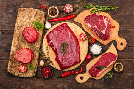 Photo for Set of various steaks with traditional spices and herbs. Fresh raw meat cuts includes ribeye, eye round, flank and striploin steaks. Old wooden background, flat lay, top view - Royalty Free Image