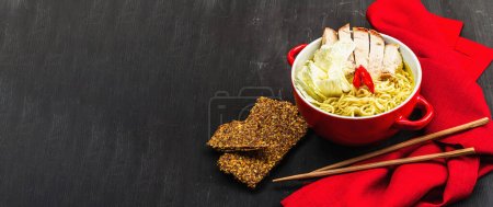 Photo for Korean noodles with baked pork, Chinese cabbage and chili pepper. Red and black design, chopsticks, wooden dark background, banner format - Royalty Free Image
