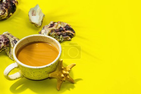 Téléchargez les photos : Une tasse de café dans un style marin. Étoile de mer, huîtres, feuilles de palmier. Lumière dure, ombre sombre, fond jaune vif, plan, espace de copie - en image libre de droit