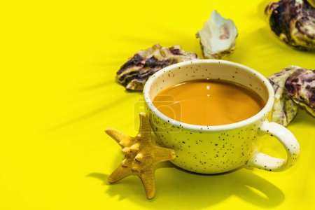 Téléchargez les photos : Une tasse de café dans un style marin. Étoile de mer, huîtres, feuilles de palmier. Lumière dure, ombre sombre, fond jaune vif, plan, espace de copie - en image libre de droit