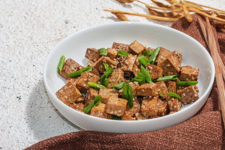 Foto de Tofu teriyaki frito con cebolletas y semillas de sésamo. Comida vegana saludable sin carne rica en proteínas y calcio. Luz dura de moda, sombra oscura, fondo de yeso, primer plano - Imagen libre de derechos