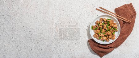 Téléchargez les photos : Tofu tériyaki frit aux oignons verts et graines de sésame. Repas végétalien sain sans viande riche en protéines et en calcium. Lumière dure tendance, ombre sombre, fond de plâtre, format de bannière - en image libre de droit