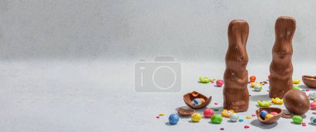 Traditionelle Ostersüßigkeiten mit Eiern, Schokohasen und festlichem Dekor. Die Suche der Kinder, trendiges hartes Licht, dunkler Schatten. Leichter Stein Betonhintergrund, flache Lage, Kopierraum
