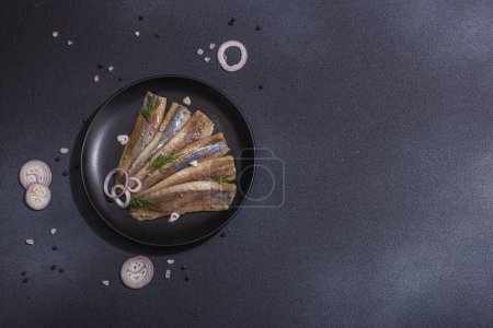 Téléchargez les photos : Filet de hareng de mer mariné mariné mariné avec échalotes et aneth. Servi prêt à manger fruits de mer, lumière dure, ombre sombre. Pierre noire fond en béton, pose plate, vue sur le dessus - en image libre de droit