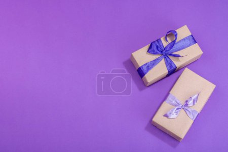 Zero waste gift concept. Wrapped in craft paper surprise box for Anniversary, Mothers or Valentines Day. Happy birthday greeting card, purple background, flat lay, top view