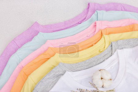 Vertical storage of clothing. Eco friendly spring closet cleaning. Pastel colored baby T-shirts, sale concept. Light stone concrete background, top view