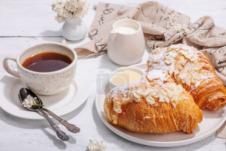 Photo for Good morning concept. Breakfast with cup of coffee and fresh croissant. Sweet creamy sauce, hard light, dark shadow. White wooden background, close up - Royalty Free Image