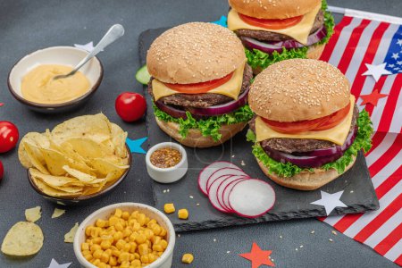 Photo for Homemade burgers. An American classic, traditional food for picnic, party or celebration Independence Day. Sauce, chips, sweet corn. Dark stone concrete background, close up - Royalty Free Image