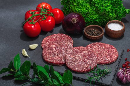 Photo for Raw burger patties. Fresh meat cutlets, spices, vegetables and herbs. Homemade American classic, traditional food for picnic, party or Independence Day. Dark stone concrete background, copy space - Royalty Free Image