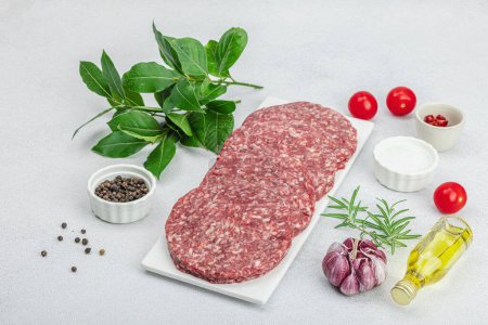 Photo for Raw burger patties. Fresh meat cutlets, spices, vegetables and herbs. Homemade American classic, traditional food for picnic, party or Independence Day. Light stone concrete background, copy space - Royalty Free Image