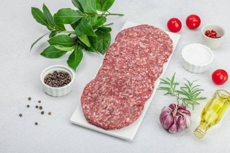 Photo for Raw burger patties. Fresh meat cutlets, spices, vegetables and herbs. Homemade American classic, traditional food for picnic, party or Independence Day. Light stone concrete background, copy space - Royalty Free Image