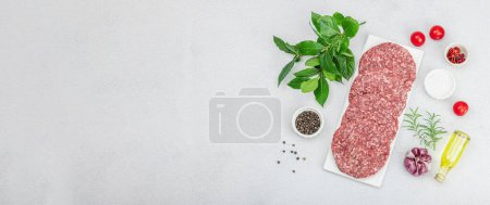 Photo for Raw burger patties. Fresh meat cutlets, spices, vegetables and herbs. Homemade American classic, traditional food for picnic, party or Independence Day. Light stone concrete background, banner format - Royalty Free Image