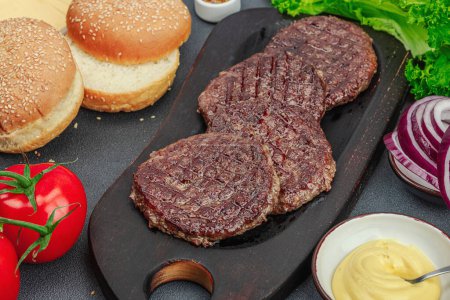 Photo for Grilled burger patties. Hot beef cutlets, buns, vegetables and sauce. Homemade American classic, traditional food for picnic, party or Independence Day. Dark stone concrete background, close up - Royalty Free Image