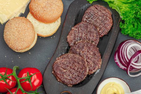 Photo for Grilled burger patties. Hot beef cutlets, buns, vegetables and sauce. Homemade American classic, traditional food for picnic, party or Independence Day. Dark stone concrete background, top view - Royalty Free Image