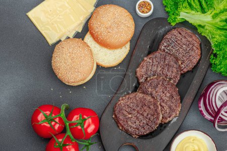 Photo for Grilled burger patties. Hot beef cutlets, buns, vegetables and sauce. Homemade American classic, traditional food for picnic, party or Independence Day. Dark stone concrete background, top view - Royalty Free Image
