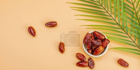 Ripe dates, a traditional Ramadan Kareem concept snack for Iftar or Suhoor meal on a light orange background. An Arabian sweet treat, palm leaves, flat lay, banner format