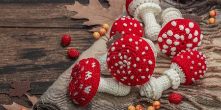 Autumn cozy mood composition. Crocheted amanita mushroom, handmade, fall hobby concept. Props and traditional decoration, knitting. Hard light, dark shadow, old wooden background, banner format