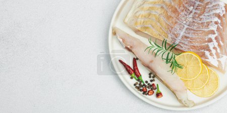 Photo for Raw pollock (Pollachius virens) fillet. Fresh fish for healthy food lifestyle. Lemon, rosemary, sea salt, chili, black peppercorn. Light stone concrete background, flat lay, banner format - Royalty Free Image