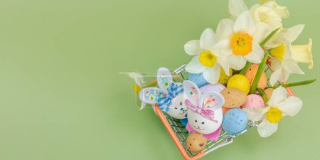 Easter sale concept. Shopping basket with festive symbols - rabbit, eggs, bird, and traditional decor. Pastel design, green background, banner format