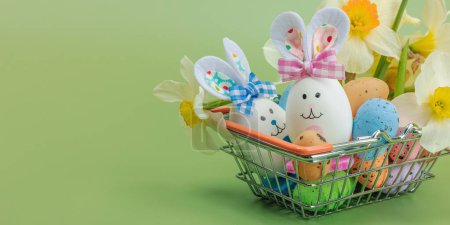 Easter sale concept. Shopping basket with festive symbols - rabbit, eggs, bird, and traditional decor. Pastel design, green background, banner format