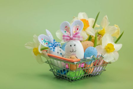 Easter sale concept. Shopping basket with festive symbols - rabbit, eggs, bird, and traditional decor. Pastel design, green background, copy space