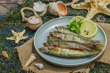 Smoked smelt with fresh lemon and herbs. Salted fish with marine decor. Trendy dish, sea rope. Blue nautical wooden background, close up