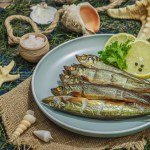 Smoked smelt with fresh lemon and herbs. Salted fish with marine decor. Trendy dish, sea rope. Blue nautical wooden background, close up