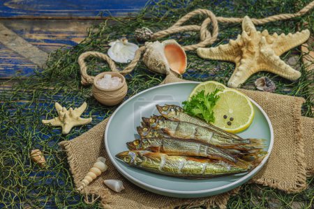 Photo for Smoked smelt with fresh lemon and herbs. Salted fish with marine decor. Trendy dish, sea rope. Blue nautical wooden background, copy space - Royalty Free Image