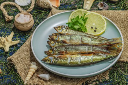 Photo for Smoked smelt with fresh lemon and herbs. Salted fish with marine decor. Trendy dish, sea rope. Blue nautical wooden background, copy space - Royalty Free Image