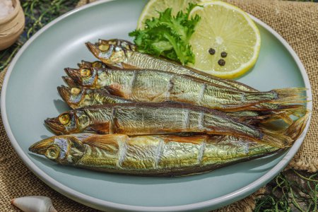 Photo for Smoked smelt with fresh lemon and herbs. Salted fish with marine decor. Trendy dish, sea rope. Blue nautical wooden background, close up - Royalty Free Image