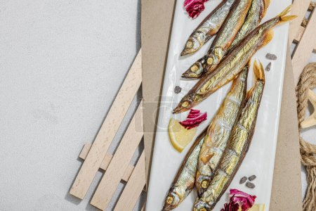 Photo for Smoked smelt with fresh lemon and herbs. Salted fish with marine decor. Trendy pallet, sea rope. Hard light, dark shadow, light stone concrete background, top view - Royalty Free Image