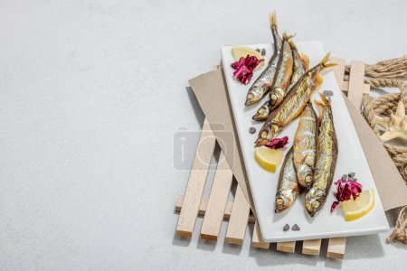 Photo for Smoked smelt with fresh lemon and herbs. Salted fish with marine decor. Trendy pallet, sea rope. Hard light, dark shadow, light stone concrete background, copy space - Royalty Free Image