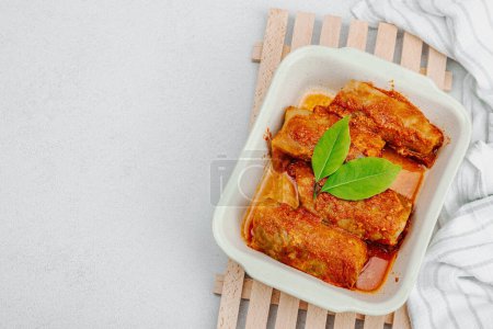Cabbage rolls stuffed with rice and meat stewed in tomato sauce. Traditional dish, ready-to-eat food, sour cream. Light stone concrete background, top view