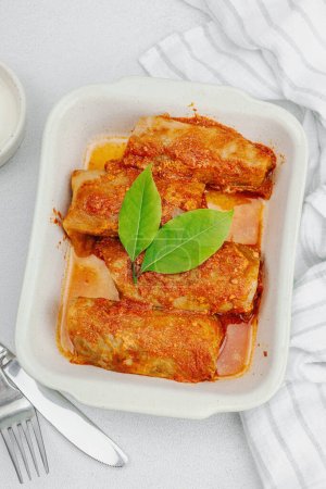 Cabbage rolls stuffed with rice and meat stewed in tomato sauce. Traditional dish, ready-to-eat food, sour cream. Light stone concrete background, top view