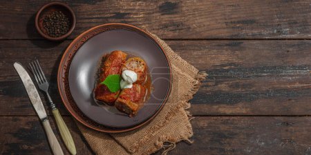 Cabbage rolls stuffed with rice and meat stewed in tomato sauce. Traditional dish, ready-to-eat food, sour cream. Old wooden background, banner format