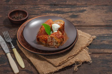 Cabbage rolls stuffed with rice and meat stewed in tomato sauce. Traditional dish, ready-to-eat food, sour cream. Old wooden background, copy space