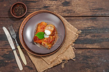 Cabbage rolls stuffed with rice and meat stewed in tomato sauce. Traditional dish, ready-to-eat food, sour cream. Old wooden background, top view