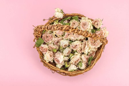 Photo for Creative composition with dry delicate roses in homemade wicker basket. Greeting card, pastel pink background, top view - Royalty Free Image