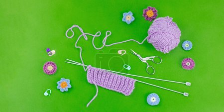 Spring knitting concept. Pattern example, traditional tools, ball of yarn, crocheted flowers. Creative handmade flat lay, bright green background, banner format