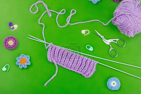 Spring knitting concept. Pattern example, traditional tools, ball of yarn, crocheted flowers. Creative handmade flat lay, bright green background, top view