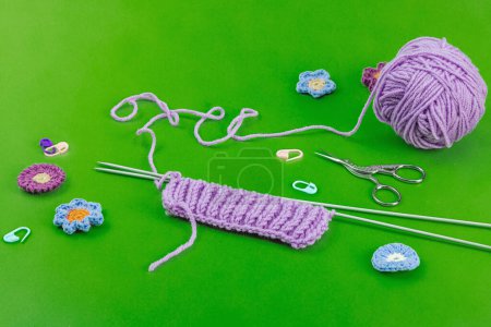 Spring knitting concept. Pattern example, traditional tools, ball of yarn, crocheted flowers. Creative handmade flat lay, bright green background, copy space