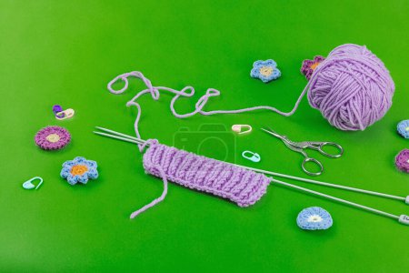 Spring knitting concept. Pattern example, traditional tools, ball of yarn, crocheted flowers. Creative handmade flat lay, bright green background, copy space